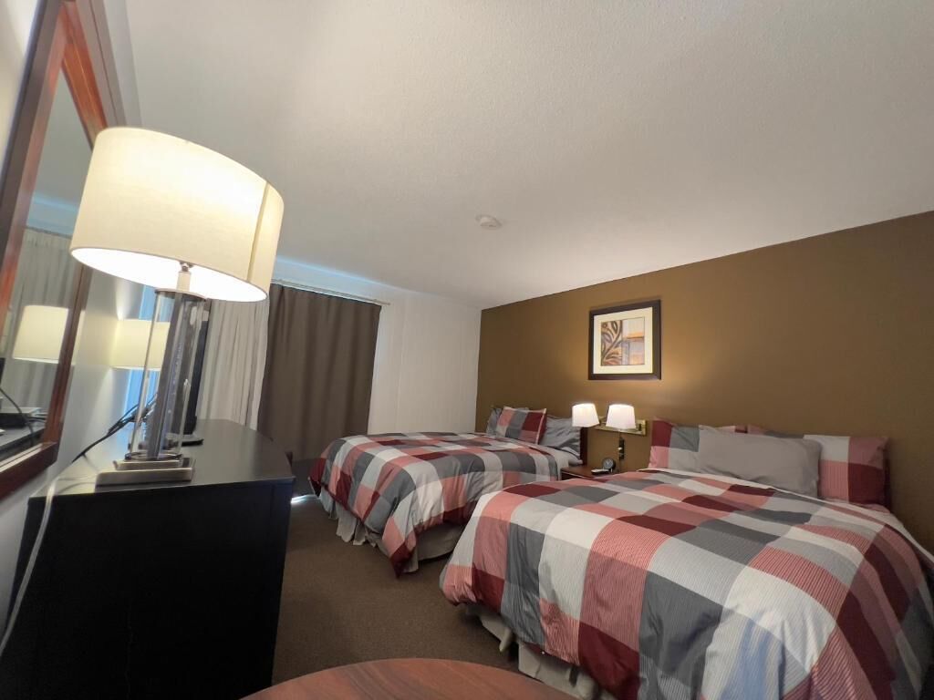 Een hotelkamer met twee bedden, een bureau, een lamp en een ingelijst schilderij aan de muur.