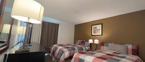 Een hotelkamer met twee bedden, een bureau, een lamp en een ingelijst schilderij aan de muur.