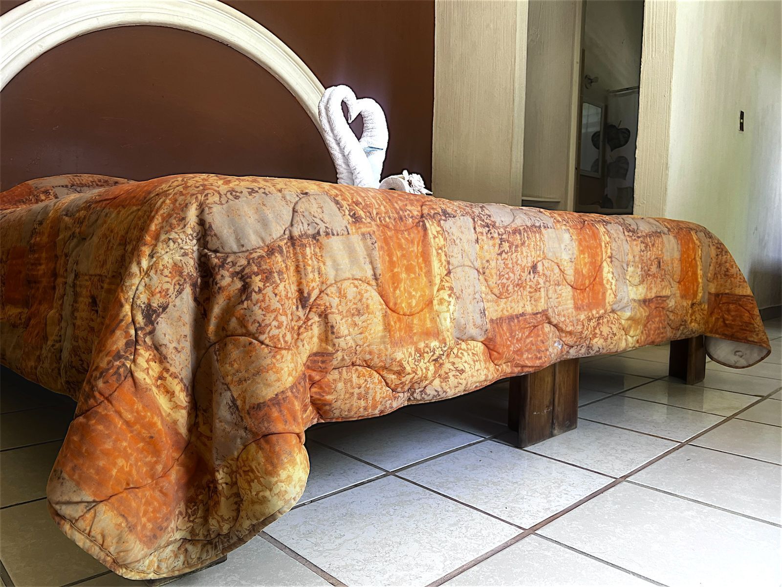 Una cama con una colcha estampada, un cojín con forma de corazón y un cabecero de madera.