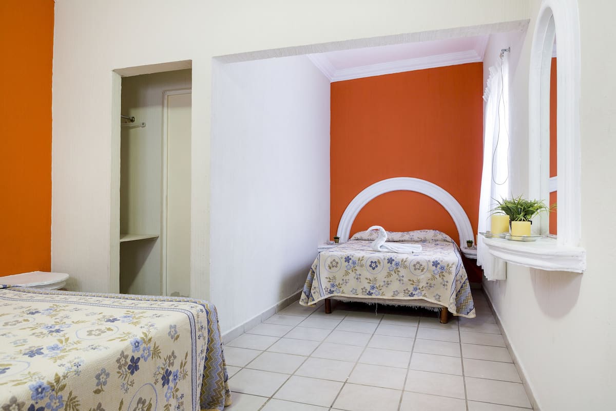 Ein Schlafzimmer mit zwei Betten, einem Fenster mit Spiegel und einer kleinen Ablage mit einer Pflanze.