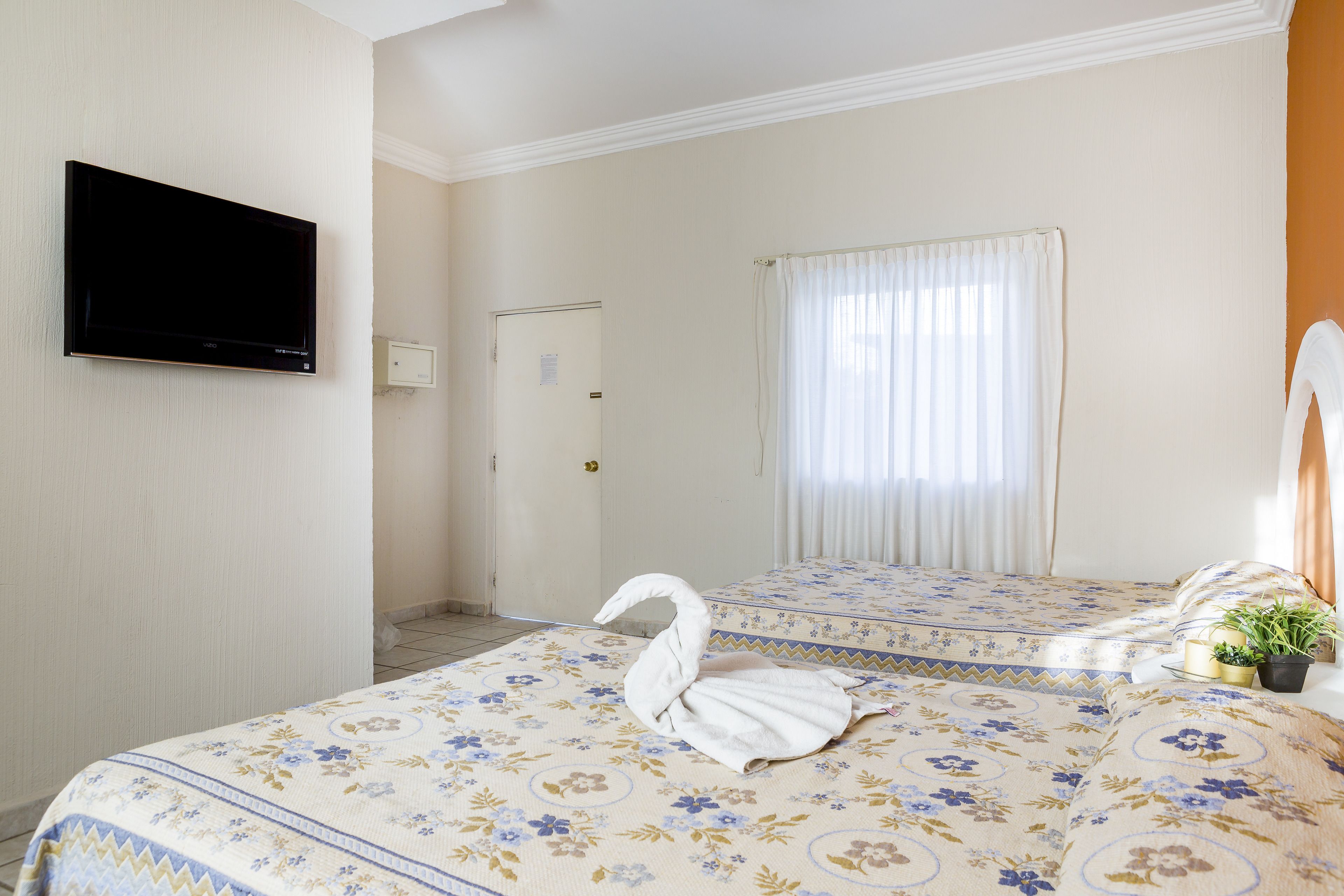 Quarto de hotel com cama, televisão de tela plana na parede, porta e janela com cortinas.