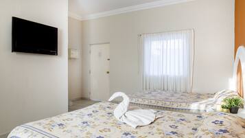 Quarto de hotel com cama, televisão de tela plana na parede, porta e janela com cortinas.