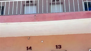 Un immeuble avec deux portes portant les numéros 14 et 13, un balcon avec une balustrade et un pot de fleurs placé devant.