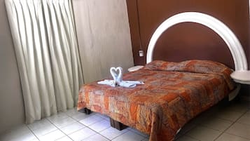 Habitación de hotel con cama, cortinas, cabecero y una disposición de toallas.
