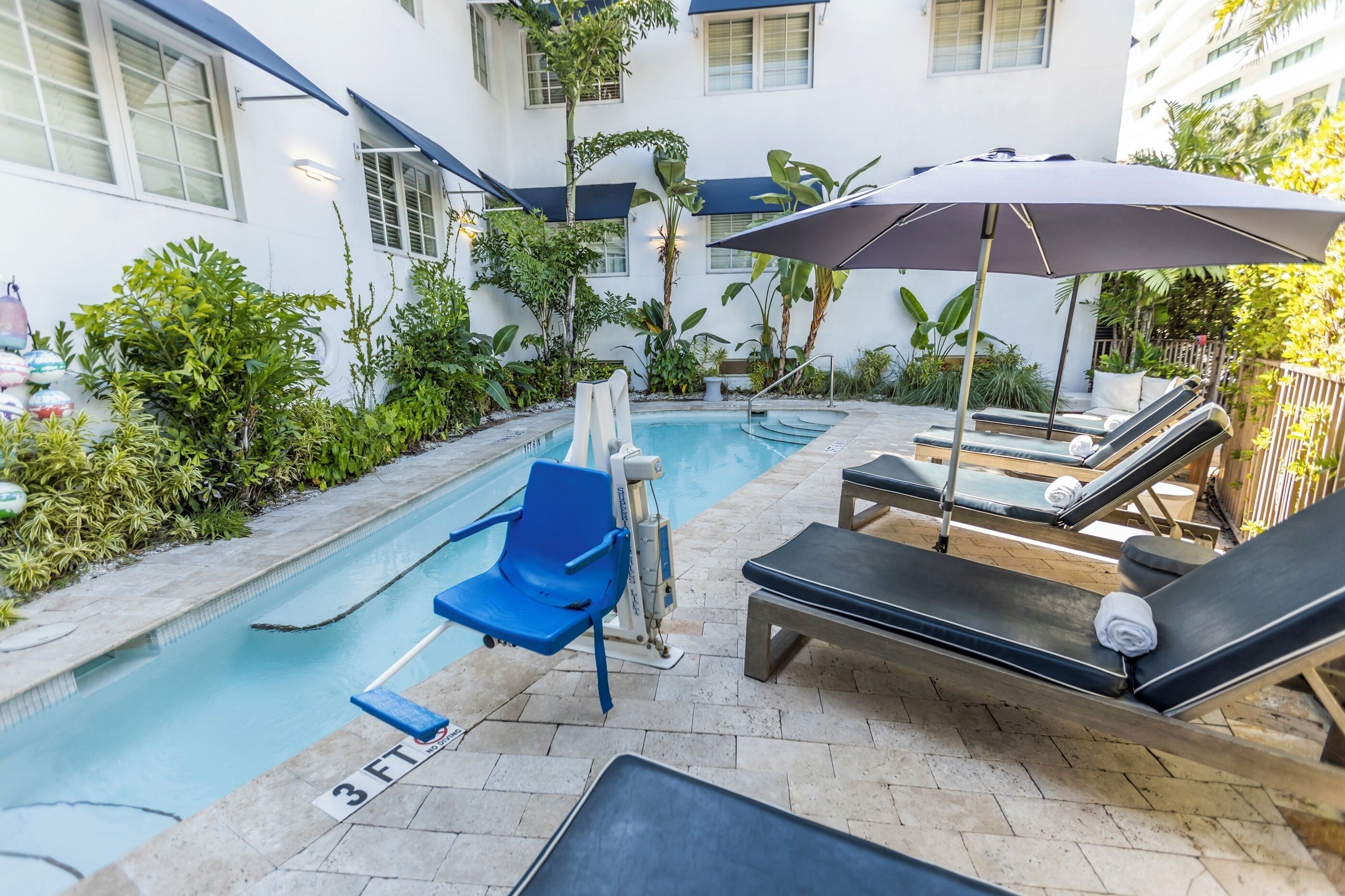 A pool area with lounge chairs, a blue chair, and an umbrella.