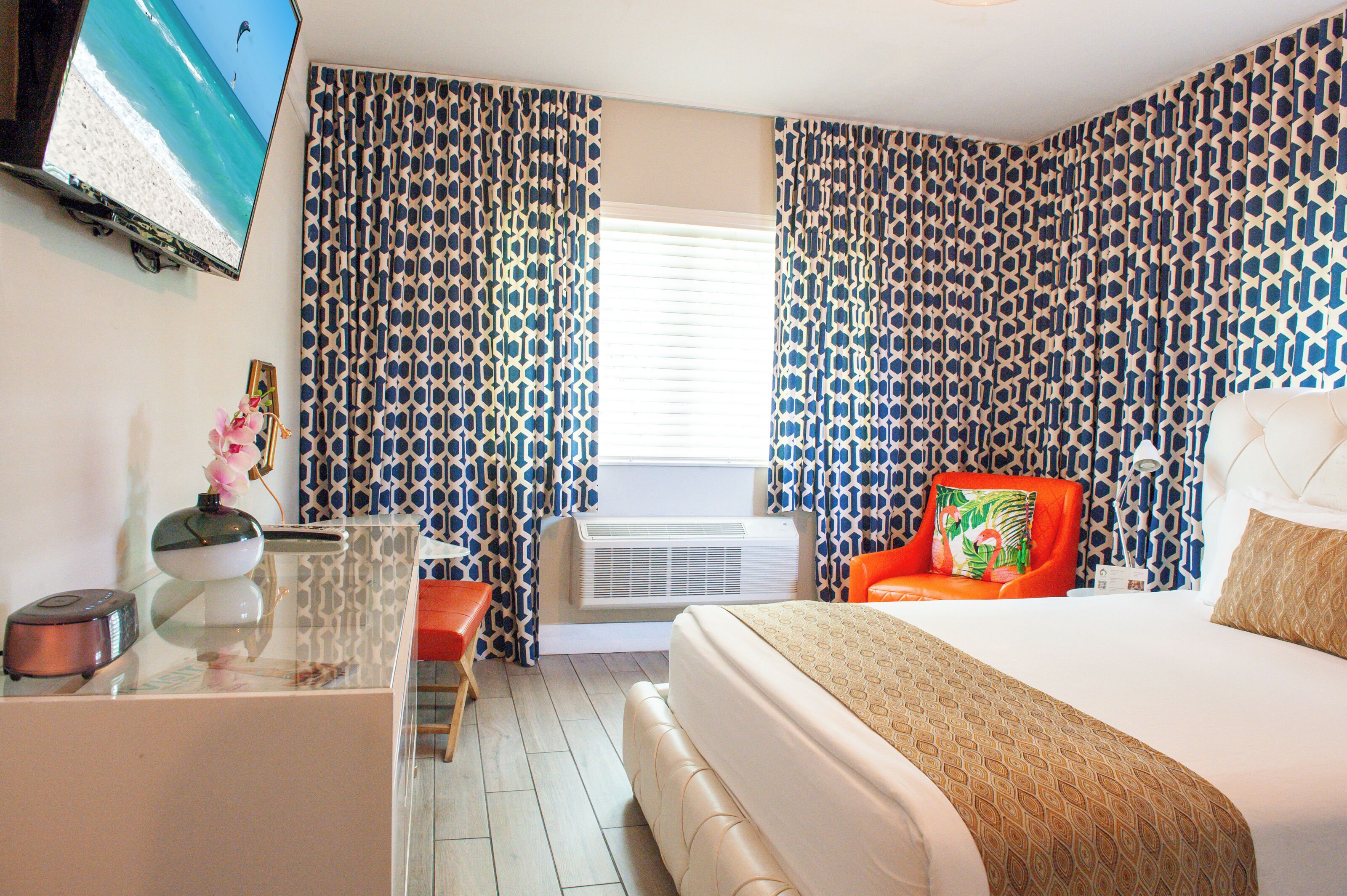 Habitación de hotel con cama, escritorio con computadora, una silla y televisor en la pared.