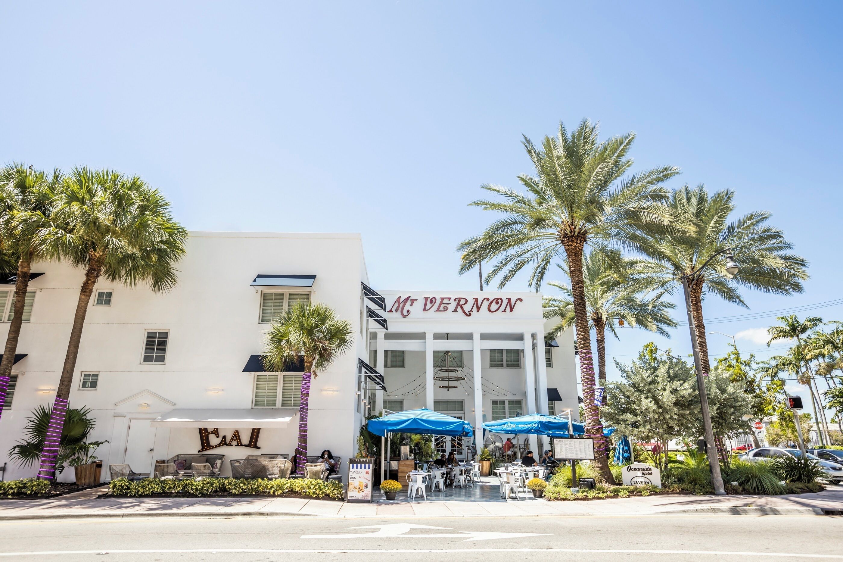 A hotel with a white facade, palm trees, and outdoor seating.