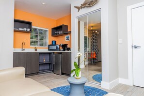 A modern kitchen with grey cabinets, a stainless steel refrigerator, and a black countertop. There is a blue rug on the floor and a white door with a fish decoration above it. - Oceanside Hotel and Suites (Miami Beach)