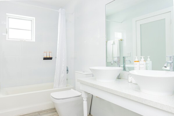 A modern bathroom with a bathtub, toilet, and two sinks.