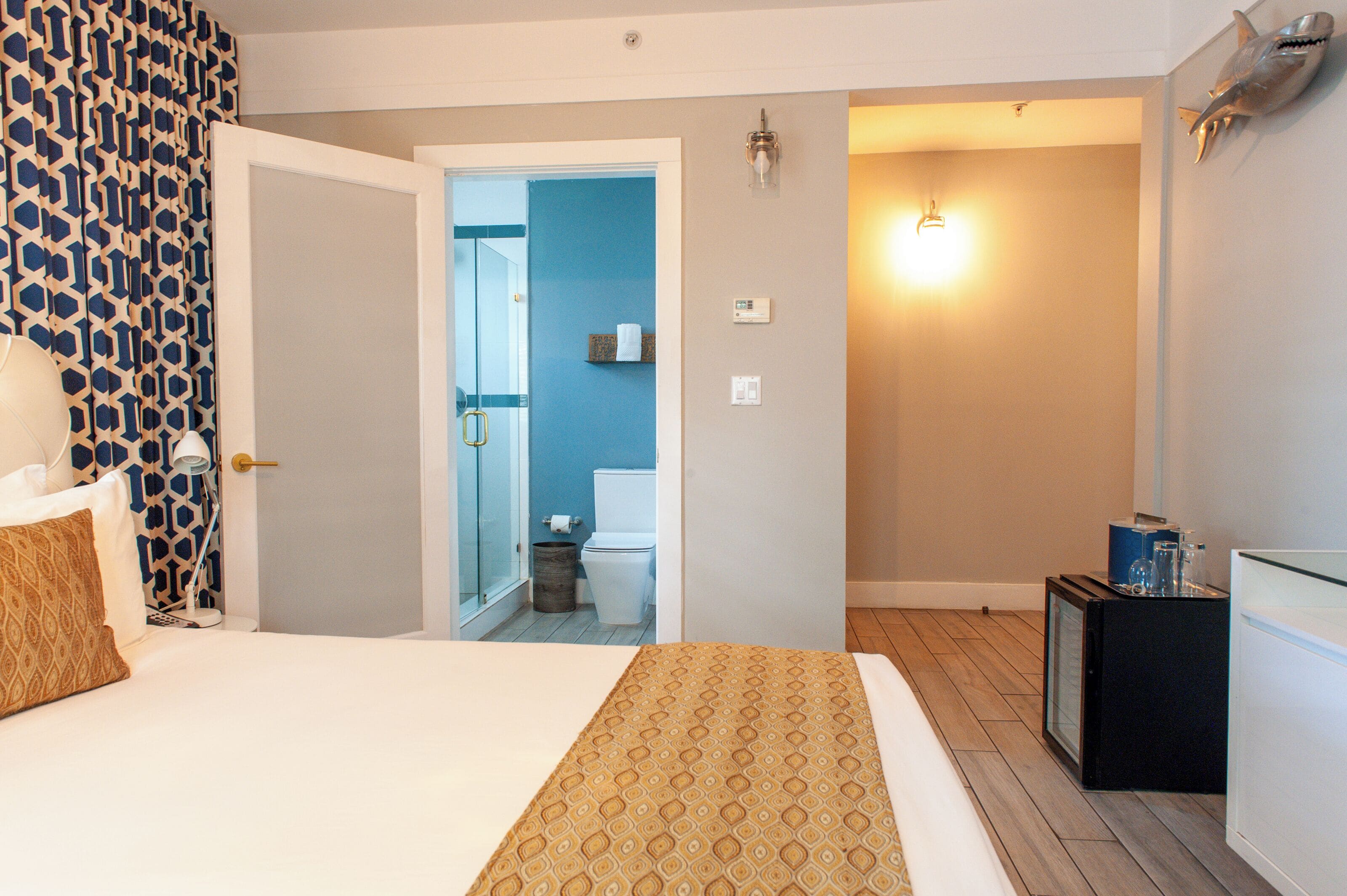 Una camera d'albergo con un letto, un comodino, uno specchio, un piccolo armadio e una porta che dà su un bagno.