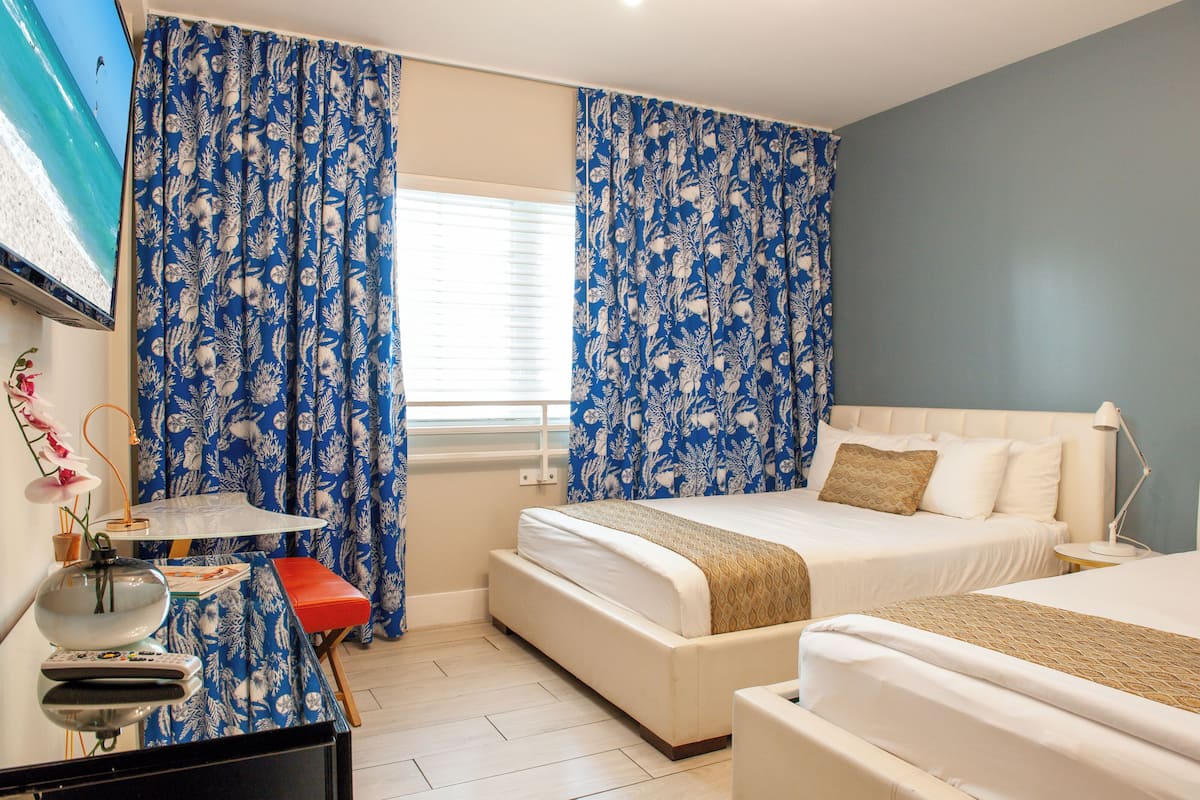 Une chambre d’hôtel avec deux lits, une télévision, un bureau et une fenêtre avec des rideaux.