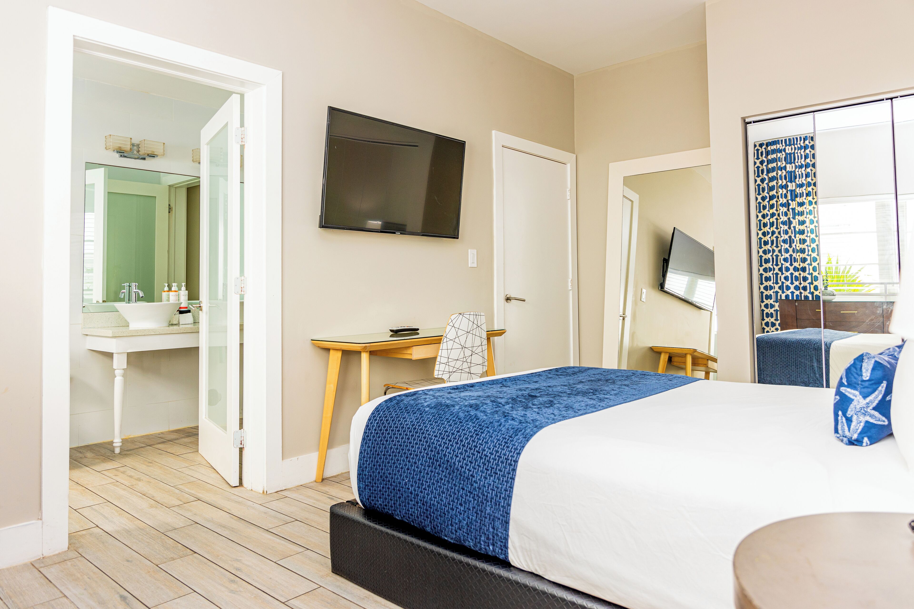 Une chambre d’hôtel équipée d’un lit, d’un bureau, d’une télévision et d’une salle de bain avec un miroir et un lavabo.