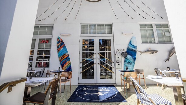 A seaside hotel entrance with a nautical theme, featuring a large door with 'TAVERN' signage, a blue and white striped flag, and shark and dolphin wall decorations. - Oceanside Hotel and Suites (Miami Beach)