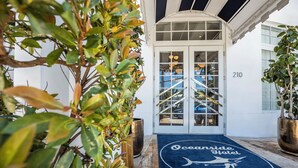 A hotel entrance with a blue mat featuring a shark logo, a double door, and a number '210' on the wall. - Oceanside Hotel and Suites (Miami Beach)