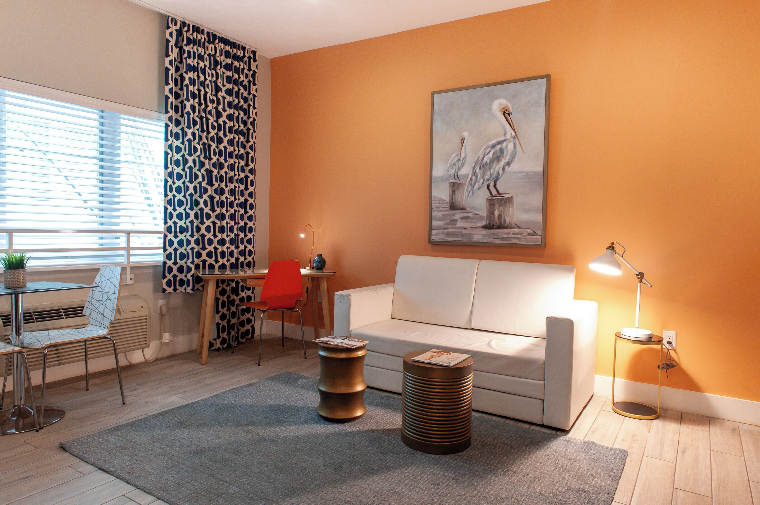 A living room with a white sofa, a red chair, a patterned curtain, a painting of birds, and a lamp.