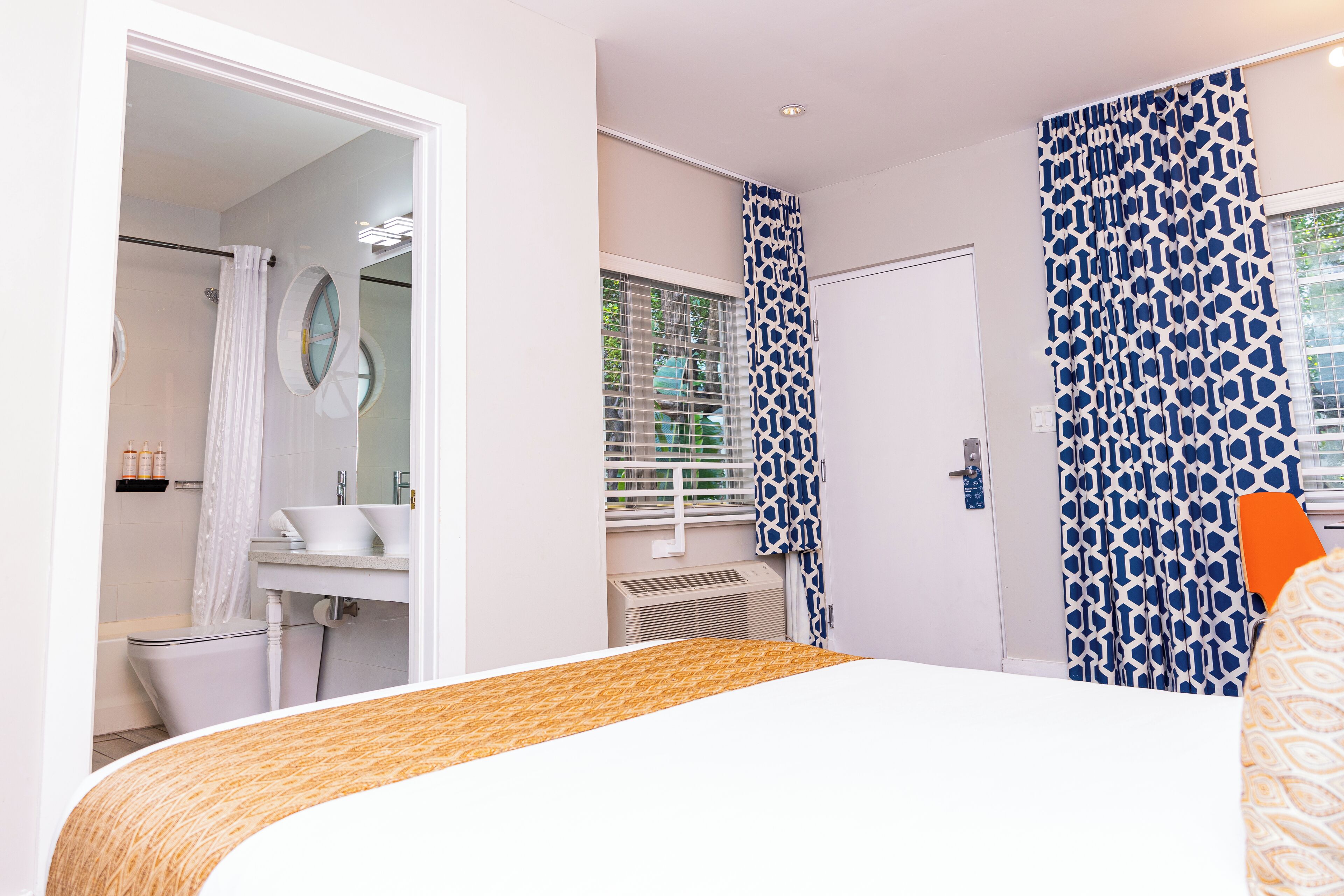 Una habitación de hotel moderna con una cama, un baño con ducha y una ventana con cortinas estampadas.