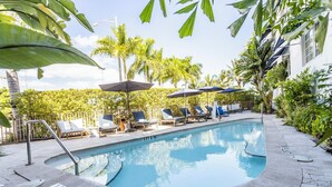 A swimming pool with lounge chairs and umbrellas, surrounded by palm trees and a fence. - Oceanside Hotel and Suites (Miami Beach)