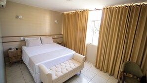 Une chambre d’hôtel avec un grand lit, une table de chevet, une chaise et une fenêtre avec des rideaux.