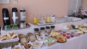 Une table de buffet proposant une variété d’aliments et de boissons, notamment des pains, des pâtisseries et des condiments.