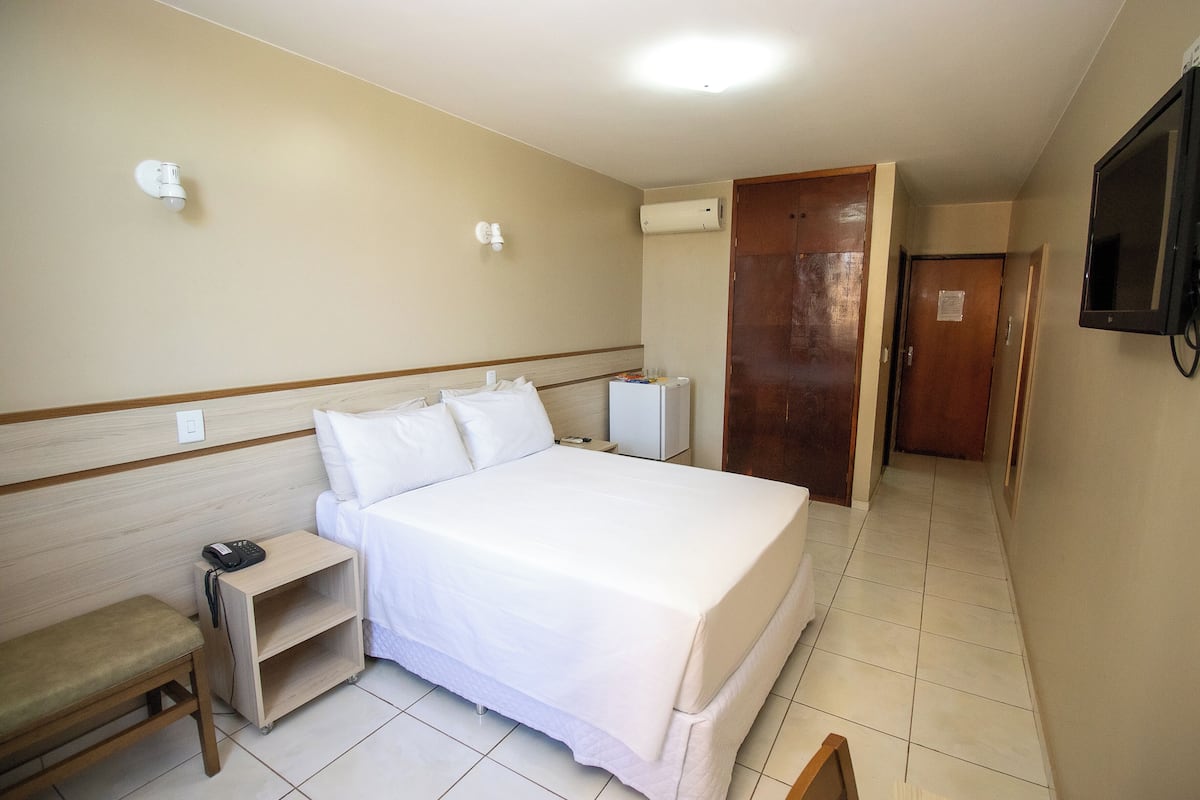 Quarto de hotel com cama, mesa de cabeceira, cadeira e televisão.
