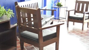 Una silla de madera con un cojín, una pequeña mesa con una planta y un fondo a rayas azul y blanco.