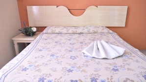 Una cama bien hecha con una colcha floral, un cabecero de madera y una mesita de noche con un jarrón de flores.