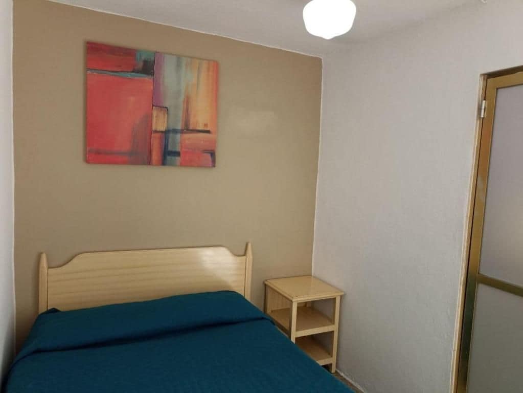 Una cama individual con cabecera, una mesita de noche pequeña y un cuadro abstracto colgado en la pared.