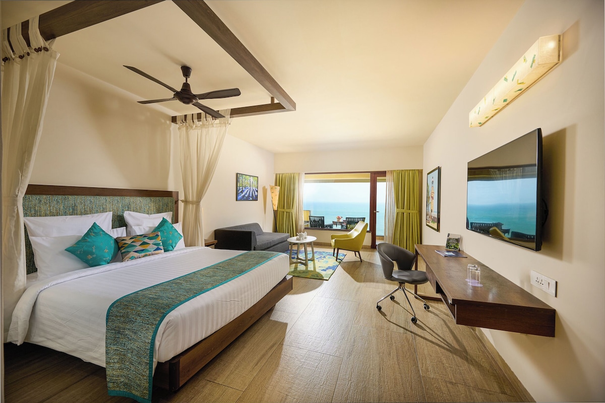 A hotel room with a bed, a desk, a chair, a TV, and a balcony with a view.