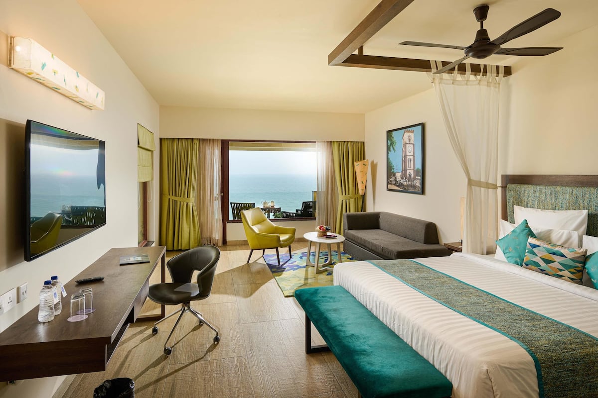 Ein Hotelzimmer mit Bett, Schreibtisch, Sessel, Sofa, Deckenventilator und Meerblick.