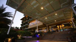 A modern hotel with a glass atrium, outdoor seating area, and a staircase leading to the entrance. - The Bheemli Resort - Managed by AccorHotels (Bhimunipatnam)
