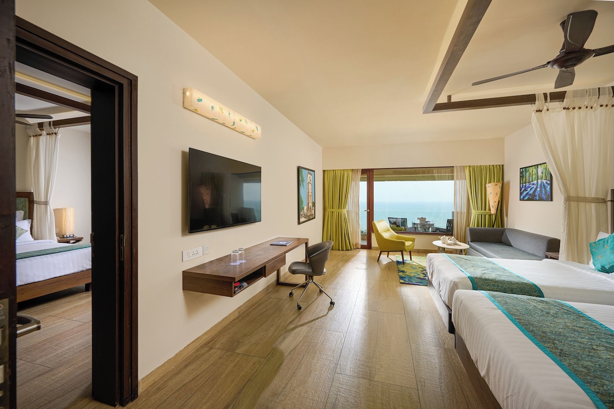 A hotel room with two beds, a desk, a TV, a chair, and a view of the ocean.