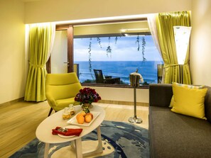 A room with a view of the ocean, a yellow armchair, a gray sofa, a small table with fruit and flowers, and a floor lamp. - The Bheemli Resort - Managed by AccorHotels (Bhimunipatnam)