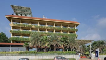A multi-story building with balconies, palm trees, and a parking area.