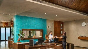 A hotel reception area with a wooden reception desk, a blue-tiled wall, and a view of the sea through large windows. - The Bheemli Resort - Managed by AccorHotels (Bhimunipatnam)