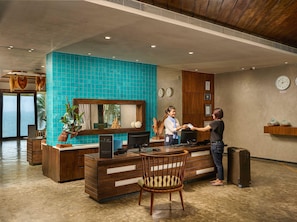 A hotel reception area with a wooden reception desk, a blue-tiled wall, and a view of the sea through large windows. - The Bheemli Resort - Managed by AccorHotels (Bhimunipatnam)