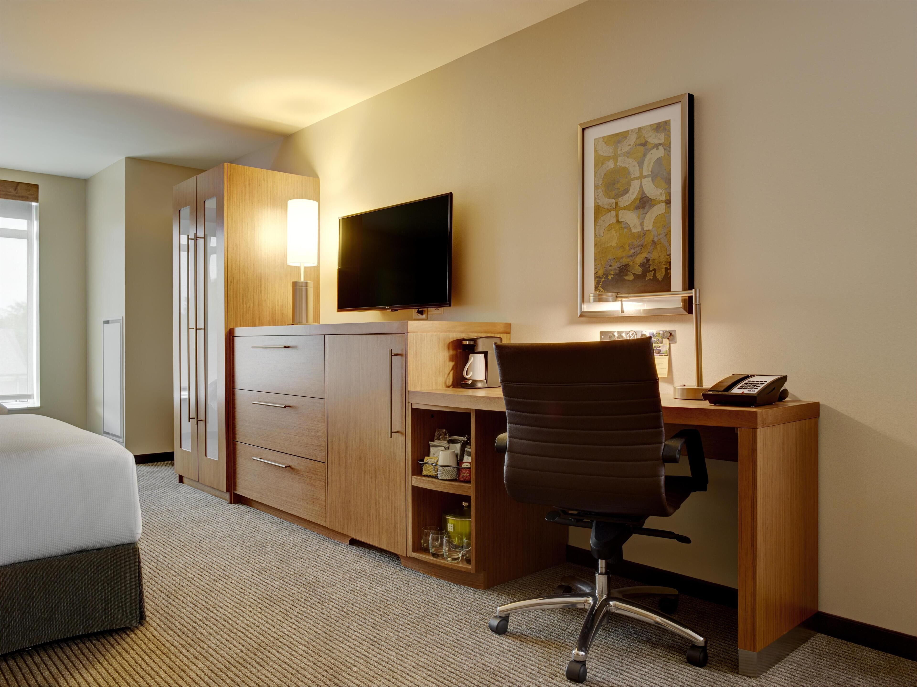 Habitación de hotel con cama, escritorio con silla, televisor, cafetera y teléfono.