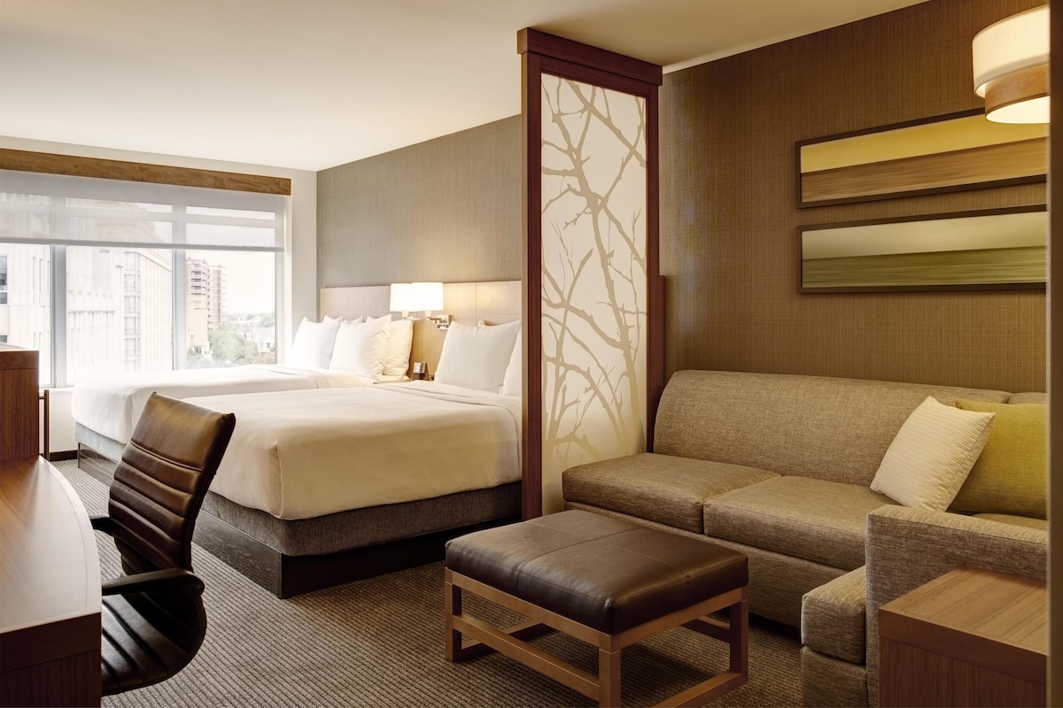 A hotel room with two beds, a sofa, a desk, and a chair.