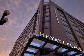 Un edificio moderno con el letrero 'HYATT PLACE', que destaca por una entrada con fachada de vidrio y una serie de luces arriba.