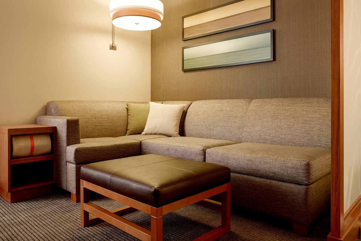 A modern living room with a sectional sofa, a wooden bench, a small wooden side table, and a wall-mounted light fixture.