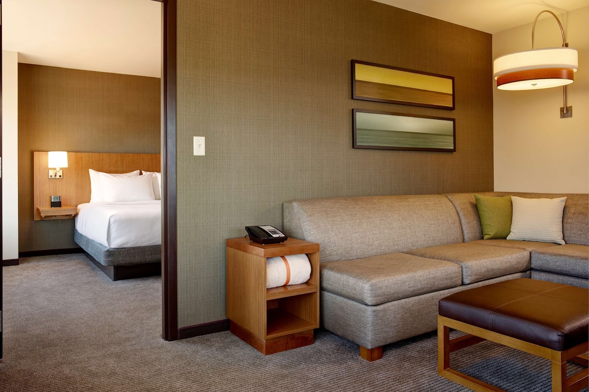 A hotel room with a bed, a sofa, a small table, and a lamp.