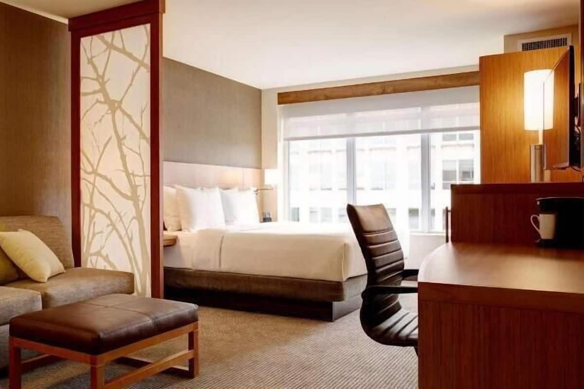 A hotel room with a bed, a sofa, a chair, a desk, and a large window.