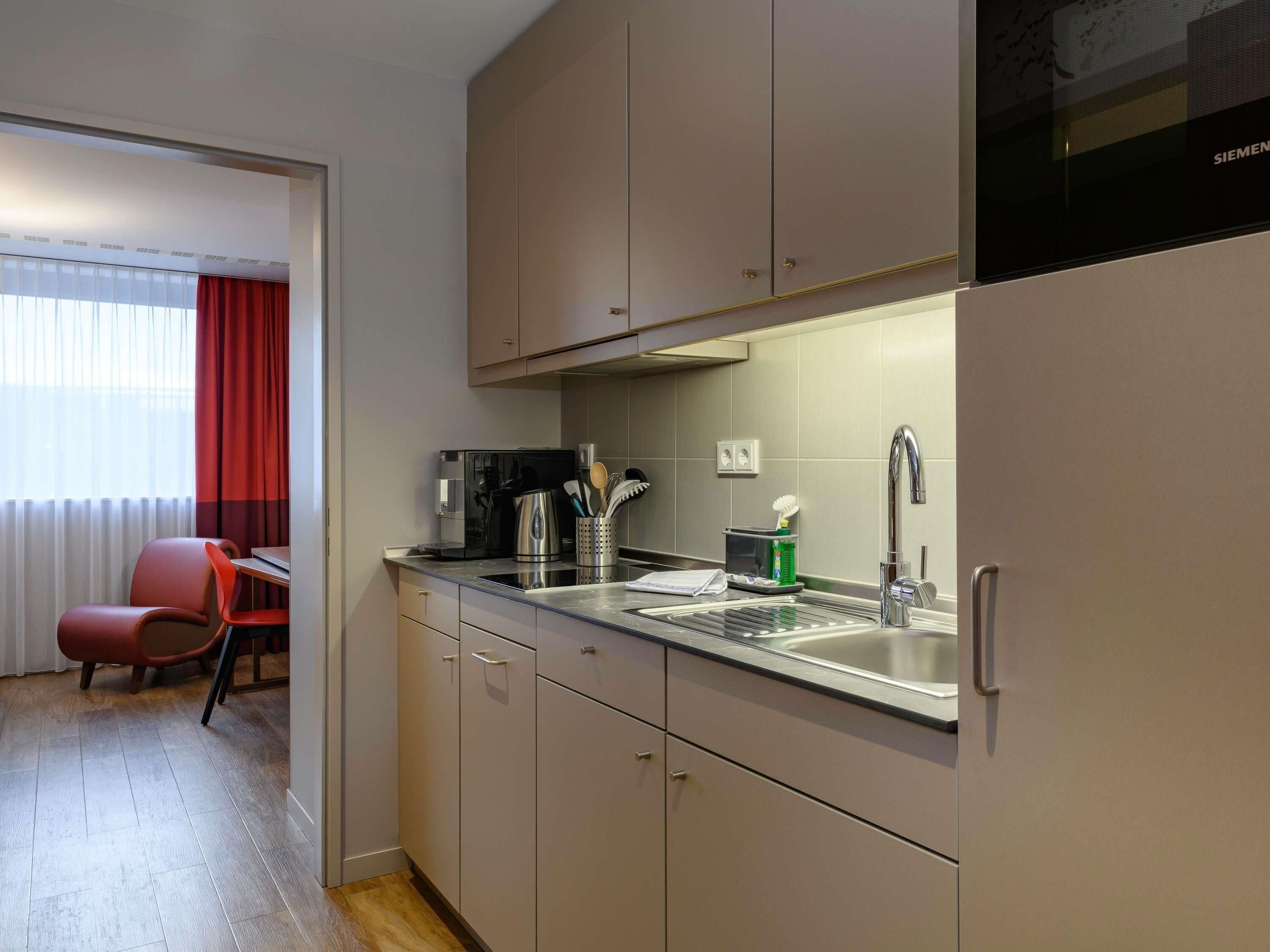 A compact kitchen with a microwave, coffee maker, and utensils, a sink with a faucet, and a chair.