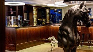 Zona de bar con armarios de madera, una gran escultura de caballo y vistas de la ciudad por la noche.