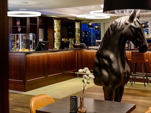 Un espace bar agrémenté de meubles en bois, d’une grande sculpture équestre et offrant une vue sur la ville de nuit.