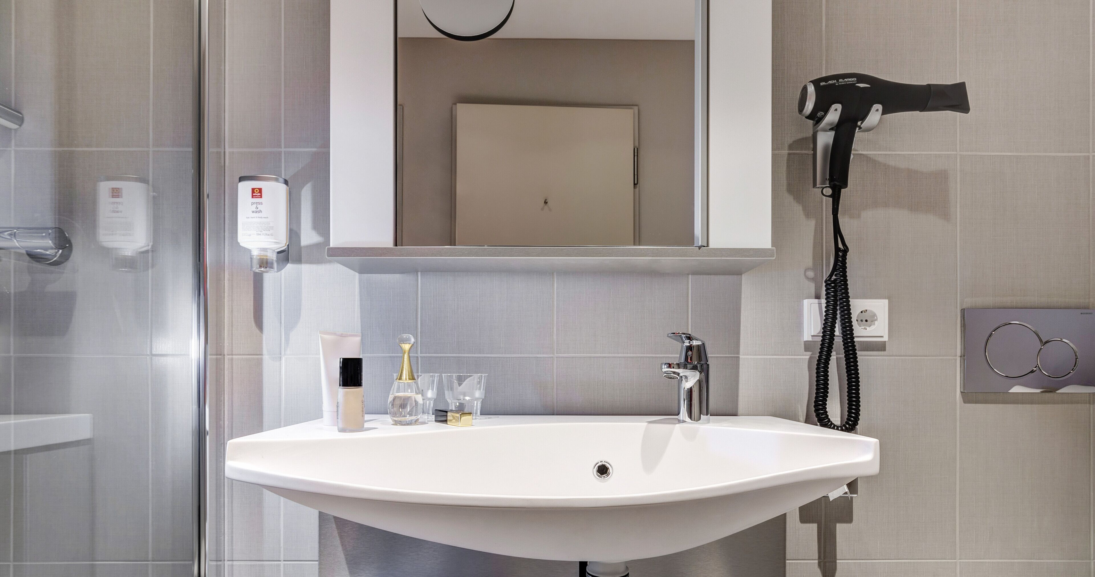 A bathroom with a white sink, a mirror, a hairdryer, and toiletries.