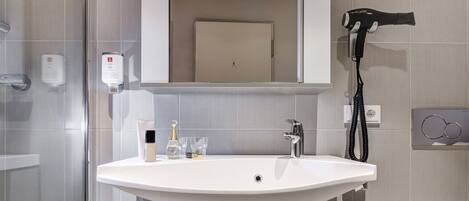 A bathroom with a white sink, a mirror, a hairdryer, and toiletries.