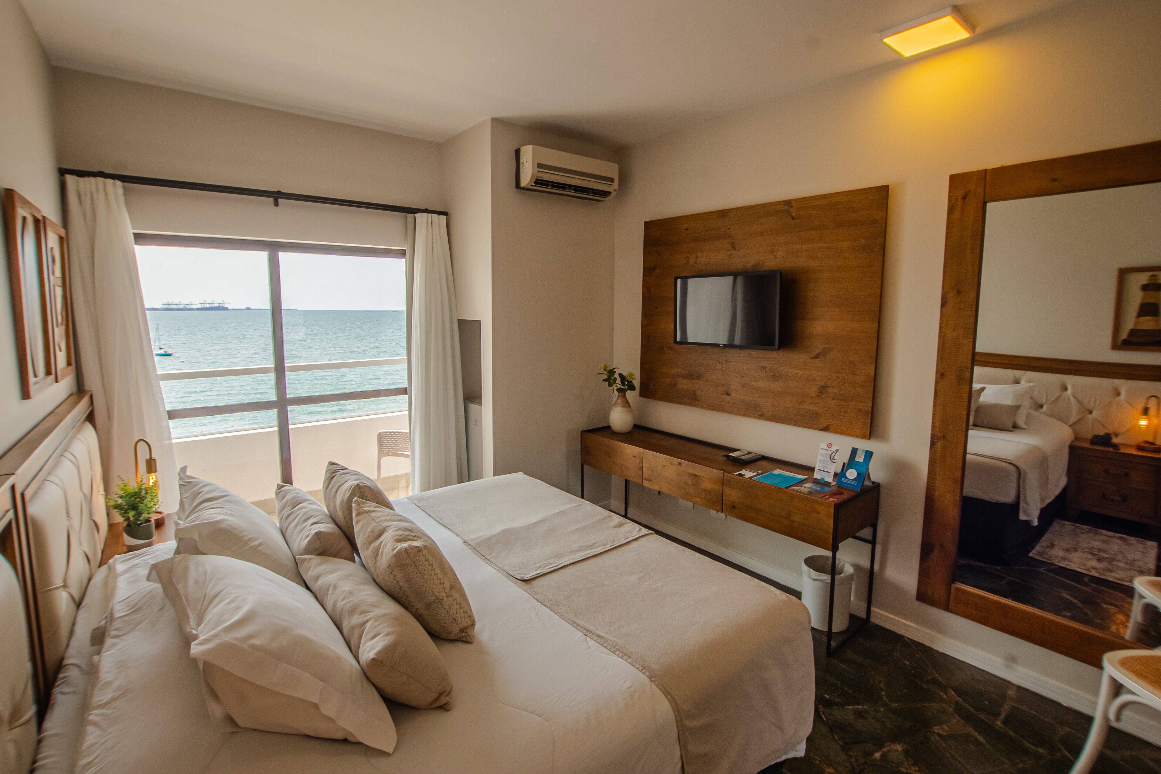 A hotel room with a bed, a desk, a TV, and a large mirror.