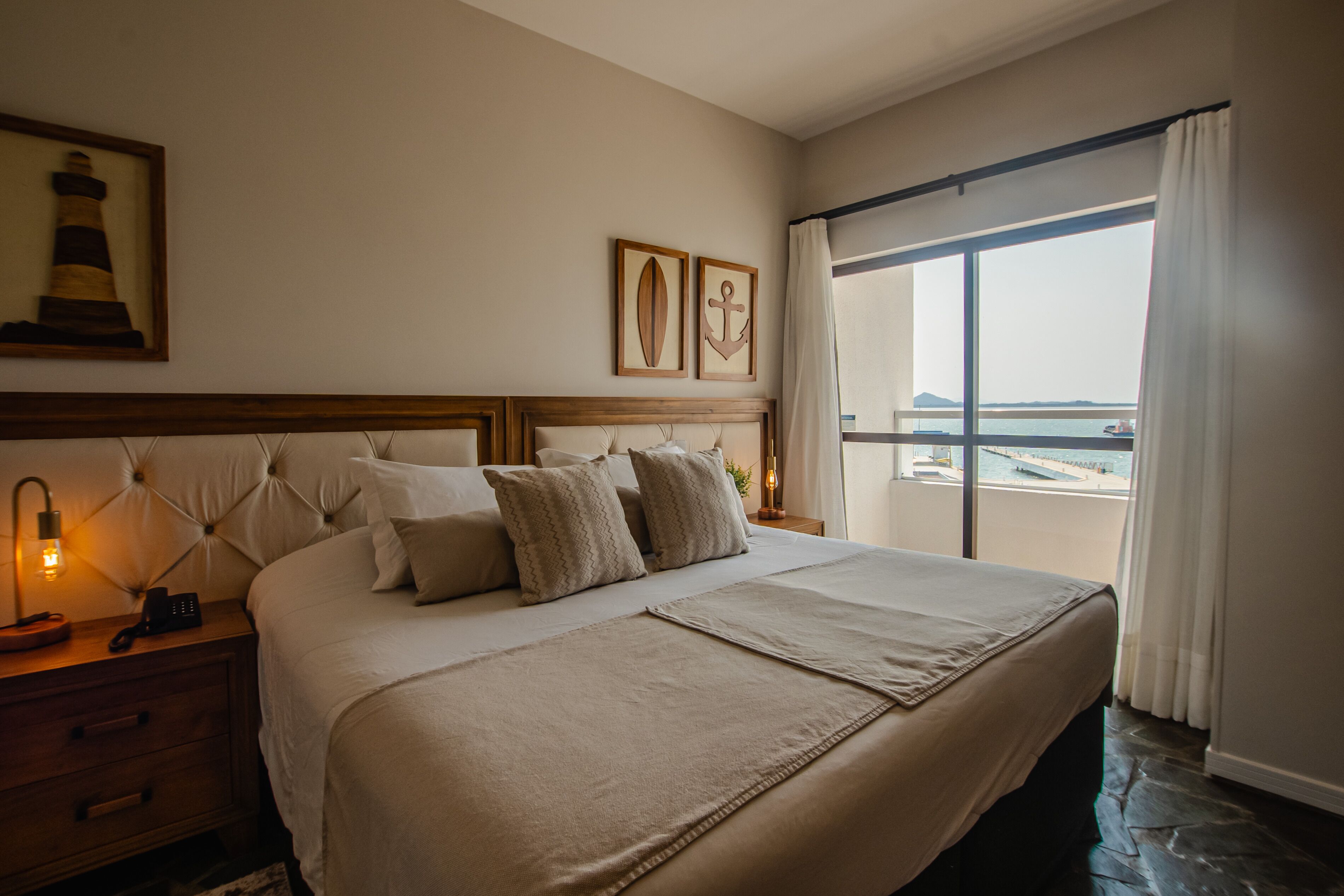 Une chambre d’hôtel avec un grand lit, une table de chevet avec une lampe et une vue sur la mer par une grande fenêtre.