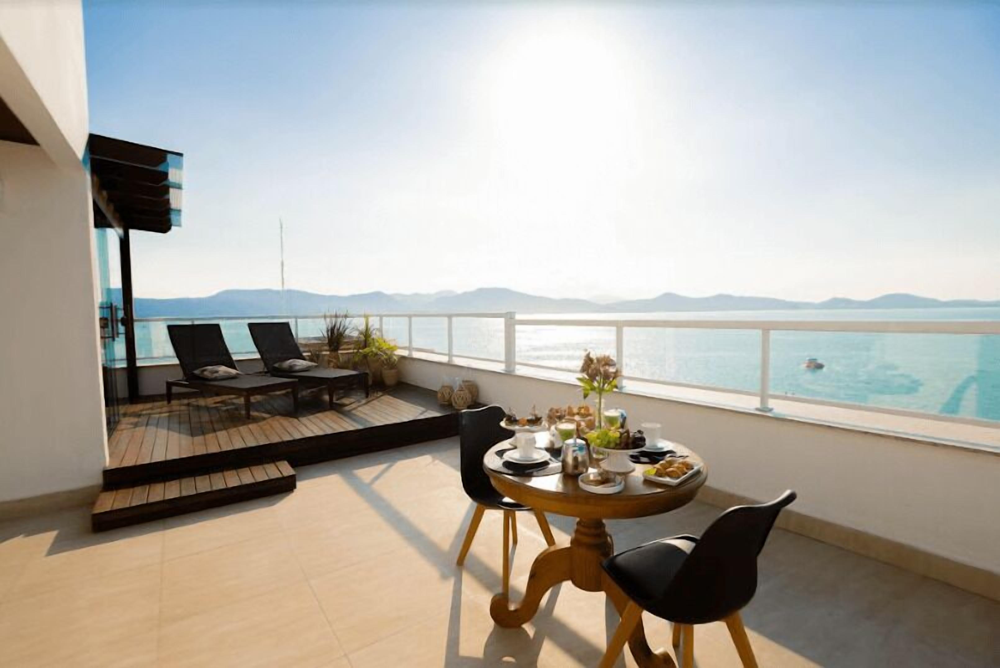 A balcony with a table set for dining, overlooking a body of water and distant mountains.