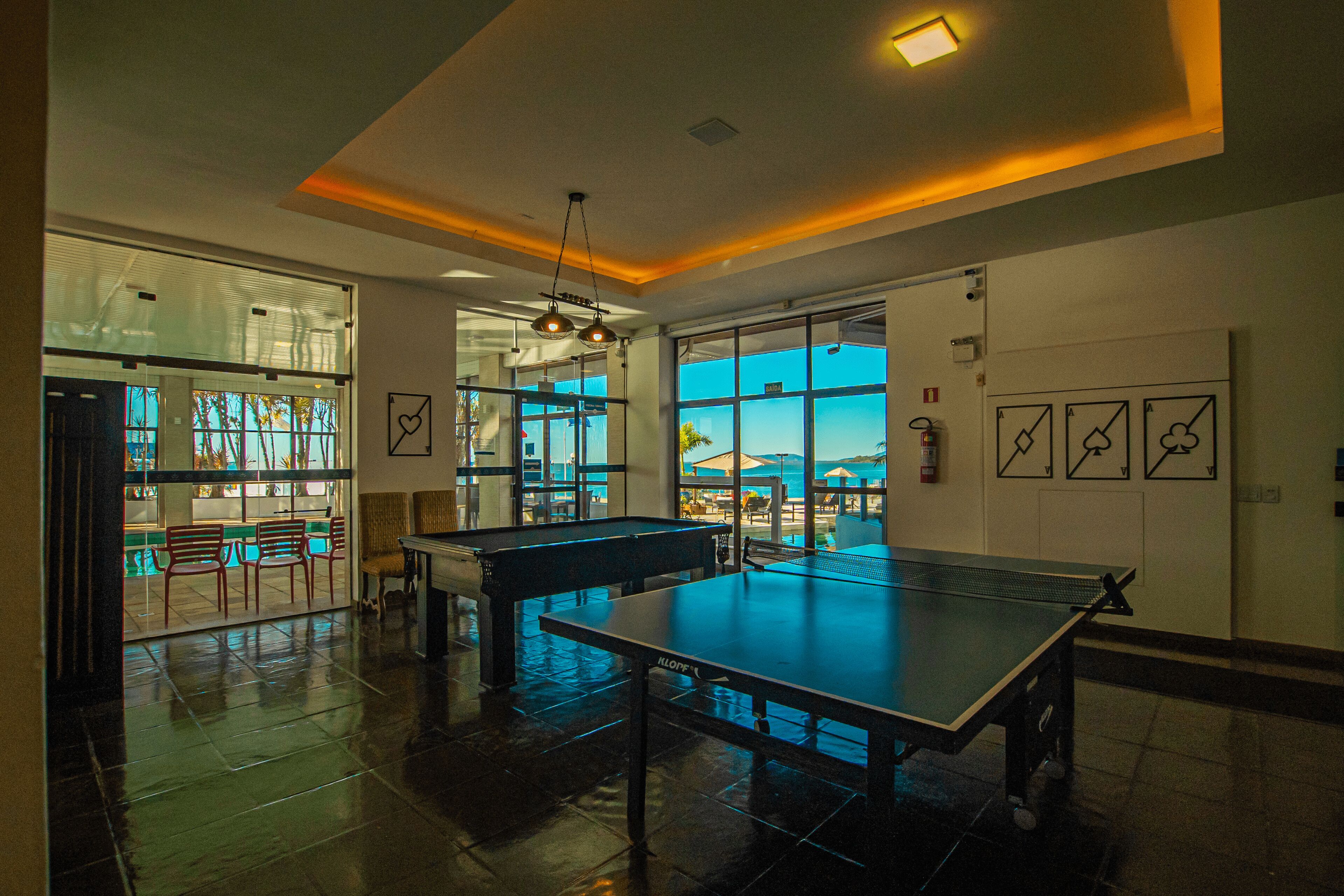 A spacious indoor area with a ping pong table, seating, and large windows offering views of the outdoors.